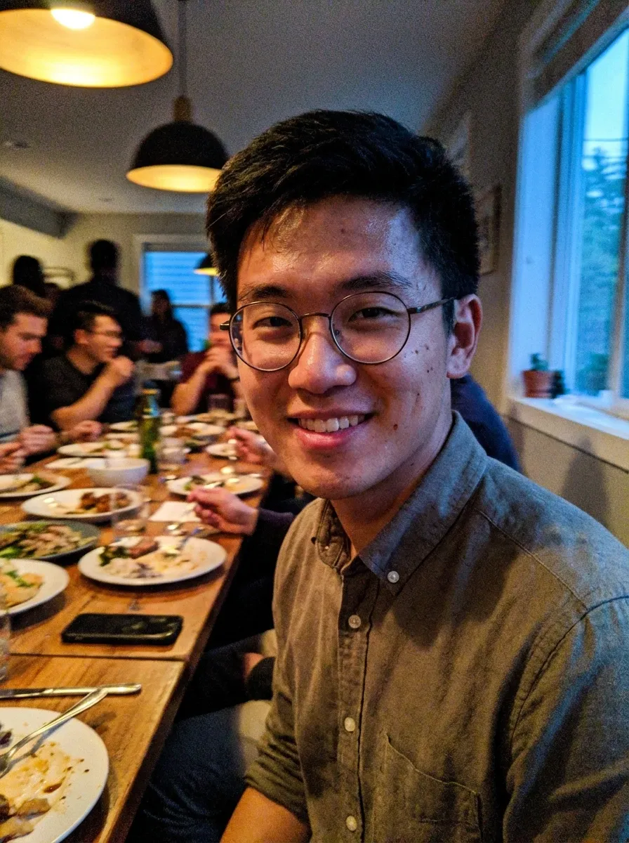 Dinner photo of a man in glasses and a gray button-down shirt seated at a long table